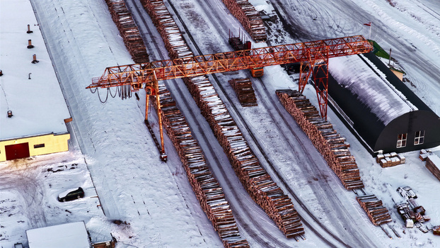 Aerial view of a lumber yard with large stacks of logs and a gantry crane in a snowy winter landscape in Latvia. Aerial view of a lumber yard with large stacks of logs and a gantry crane in a snowy winter landscape in Latvia.