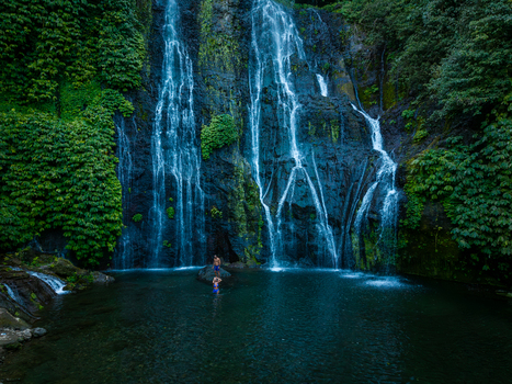 Aerial view of Banyumala Waterfall with lush green vegetation on the rocky cliff and people swimming in the clear pool in Sukasada Bali Indonesia.
