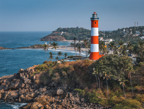 Aerial view of Vizhinjam Lighthouse on a rocky cliff overlooking the blue ocean and sandy beach with palm trees Kovalam Kerala India. Aerial view of Vizhinjam Lighthouse on a rocky cliff overlooking the blue ocean and sandy beach with palm trees Kovalam Kerala India.