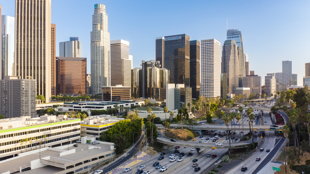 Aerial view of the Los Angeles skyline featuring skyscrapers modern office buildings and a busy highway interchange with cars during the day in Los Angeles California United States.