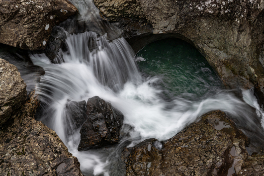 View of the Fairy Pools waterfall cascading over dark volcanic rocks into a clear green natural basin in Isle of Skye Scotland United Kingdom.