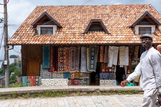 Kruje Albania 12 June 2026 View of a traditional wooden shop displaying colorful handmade carpets under a tiled roof with a man walking on the cobblestone street.