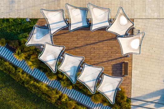 Aerial view of modern tensile fabric shades arranged in a circular pattern over a wooden deck in a park in Plock Mazowieckie Voivodeship Poland. Aerial view of modern tensile fabric shades arranged in a circular pattern over a wooden deck in a park in Plock Mazowieckie Voivodeship Poland.