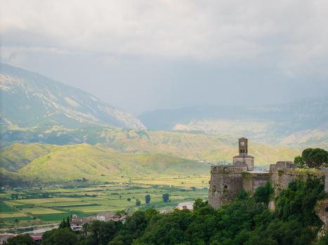 Aerial view of Gjirokaster Fortress with its iconic clock tower and ancient stone walls overlooking the green valley and mountains in Gjirokaster Gjirokaster County Albania. Aerial view of Gjirokaster Fortress with its iconic clock tower and ancient stone walls overlooking the green valley and mountains in Gjirokaster Gjirokaster County Albania.
