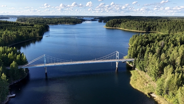 Aerial view of Potkusalmen silta Bridge spanning a calm lake surrounded by dense pine forests under a bright blue sky in Savonlinna Etela Savo Finland. Aerial view of Potkusalmen silta Bridge spanning a calm lake surrounded by dense pine forests under a bright blue sky in Savonlinna Etela Savo Finland.