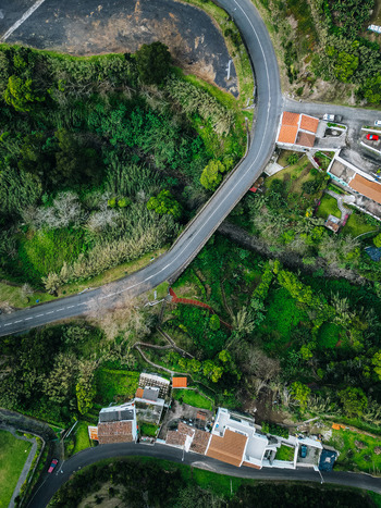 Aerial view of a curving road cutting through dense green foliage near buildings the town s structures contrasting with the natural landscape Agua de Alto Azores Portugal.