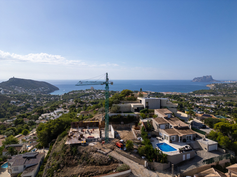 Aerial view of a construction site with a crane modern villas with swimming pools and coastal landscape in Moraira Valencian Community Spain.