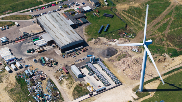 Aerial view of Chelveston Wind Farm featuring a large wind turbine next to an industrial warehouse and parking lot in Wellingborough England United Kingdom. Aerial view of Chelveston Wind Farm featuring a large wind turbine next to an industrial warehouse and parking lot in Wellingborough England United Kingdom.