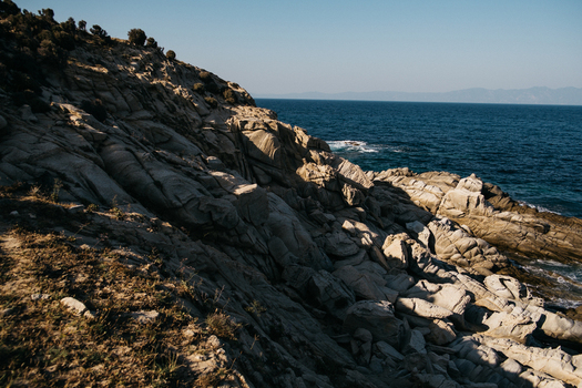 View of the rugged rocky coastline of Neos Marmaras with deep blue sea and golden hour light in Neos Marmaras Greece.