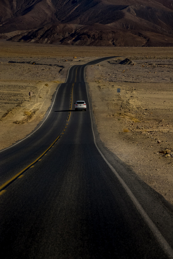 View of a white car driving on a winding road through the arid desert landscape of Death Valley National Park with rugged mountains in Death Valley California United States.