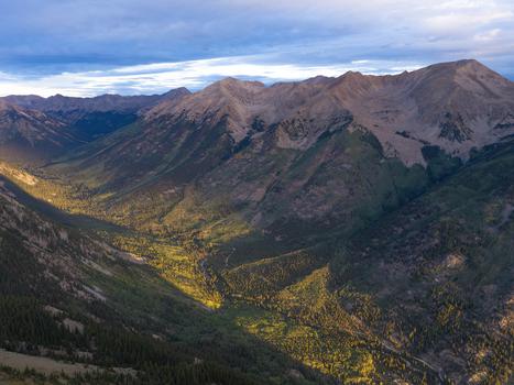 Aerial view of Missouri Mountain and the lush Missouri Gulch valley illuminated by morning light with rugged peaks and evergreen forests in Buena Vista Colorado United States.