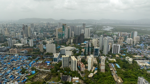 Aerial view of Dharavi Slums with its dense blue roofed structures contrasting with the modern high rise skyline and lush green patches in the background in Mumbai Maharashtra India. Aerial view of Dharavi Slums with its dense blue roofed structures contrasting with the modern high rise skyline and lush green patches in the background in Mumbai Maharashtra India.