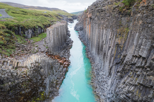 Aerial view of Studlagil Canyon with turquoise glacial water flowing between towering basalt columns and green hills Eiriksstadhir Mulathing Iceland. Aerial view of Studlagil Canyon with turquoise glacial water flowing between towering basalt columns and green hills Eiriksstadhir Mulathing Iceland.
