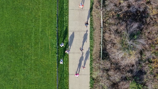 Aerial view of people walking along a concrete path between a green grass field and dry brush in Boulder Colorado United States. Aerial view of people walking along a concrete path between a green grass field and dry brush in Boulder Colorado United States.