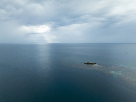 Aerial view of an islet surrounded by turquoise shallows amidst the deep blue sea under a sky streaked with sunlight Karimunjawa Central Java Indonesia.