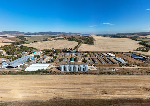 Aerial view of silos and grain storage facilities near Paszto Nograd County Hungary surrounded by summer crop fields farmland and rural hills in an agricultural landscape. Aerial view of silos and grain storage facilities near Paszto Nograd County Hungary surrounded by summer crop fields farmland and rural hills in an agricultural landscape.