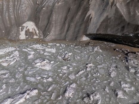Aerial view of a glacial lake filled with floating ice chunks and debris situated at the base of a steep dark rocky mountain slope Nepal.