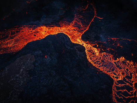Aerial view of a glowing lava flow cutting through dark volcanic rock in Iceland. Aerial view of a glowing lava flow cutting through dark volcanic rock in Iceland.