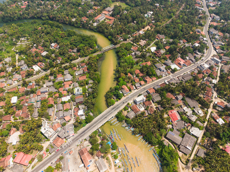 Aerial view of a river winding through a coastal town with lush tropical trees residential houses and a road bridge in Dodanduwa Southern Province Sri Lanka. Aerial view of a river winding through a coastal town with lush tropical trees residential houses and a road bridge in Dodanduwa Southern Province Sri Lanka.