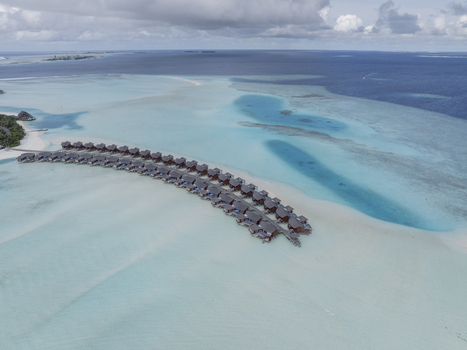 Aerial view of overwater bungalows arranged in a row over a turquoise lagoon with wooden walkways and deep blue ocean in the background in Maldives. Aerial view of overwater bungalows arranged in a row over a turquoise lagoon with wooden walkways and deep blue ocean in the background in Maldives.