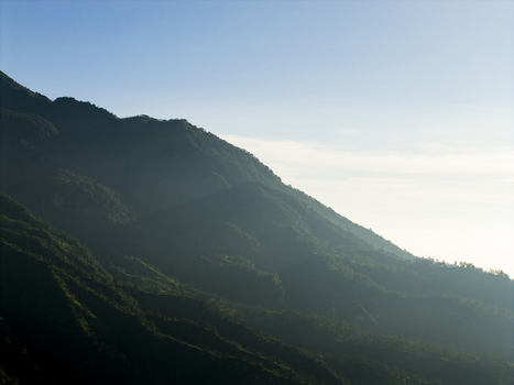 Aerial view of the lush green slopes of Mount Merapi shrouded in light morning mist under a clear blue sky near Kecamatan Pakem Daerah Istimewa Yogya Indonesia. Aerial view of the lush green slopes of Mount Merapi shrouded in light morning mist under a clear blue sky near Kecamatan Pakem Daerah Istimewa Yogya Indonesia.
