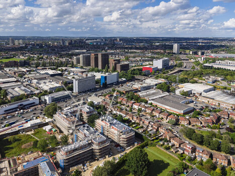 Aerial view of a residential construction site with cranes and scaffolding surrounded by suburban housing industrial buildings and green spaces in London England United Kingdom. Aerial view of a residential construction site with cranes and scaffolding surrounded by suburban housing industrial buildings and green spaces in London England United Kingdom.