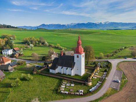 Aerial view of the historic Church of St. Ladislaus with its red onion dome and stone walls surrounded by green fields and the Tatra Mountains in Liptovske Matiasovce Zilina Region Slovakia.