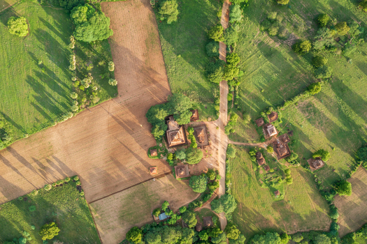 Aerial view of ancient Buddhist temples and pagodas scattered across lush green fields and dirt paths under warm sunlight in Old Bagan Mandalay Region Myanmar Burma. Aerial view of ancient Buddhist temples and pagodas scattered across lush green fields and dirt paths under warm sunlight in Old Bagan Mandalay Region Myanmar Burma.
