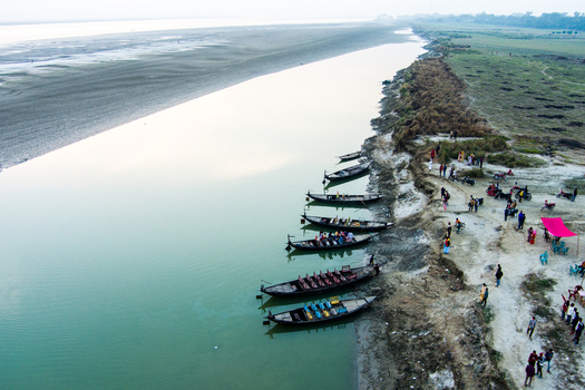 Aerial view of wooden boats moored along the riverbank with people gathered on the sandy shore in Rajshahi Rajshahi Division Bangladesh.