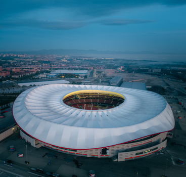 Aerial view of Riyadh Air Metropolitano Stadium with its distinctive white roof and illuminated interior bowl set against the urban landscape of Madrid Comunidad de Madrid Spain.