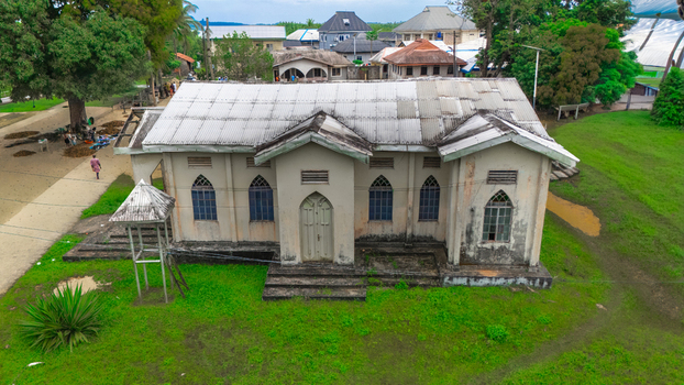 Aerial view of a historic church building with arched windows and a corrugated metal roof surrounded by green lawns and trees in Minima Rivers Nigeria.