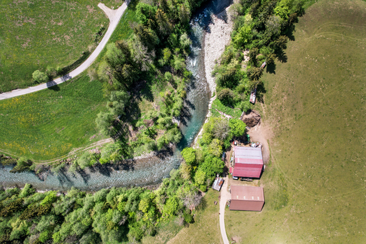 Aerial view of a winding river flowing through lush green meadows and dense forests near farm buildings in Rougemont Vaud Switzerland. Aerial view of a winding river flowing through lush green meadows and dense forests near farm buildings in Rougemont Vaud Switzerland.