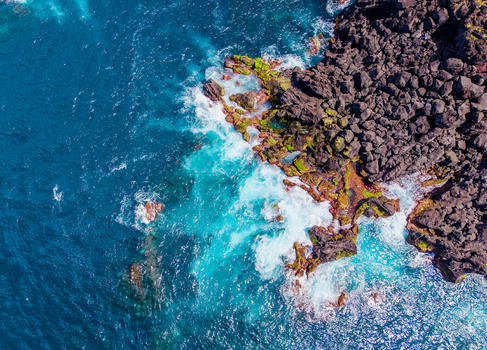 Aerial view of the rugged dark volcanic coastline kissed by the turquoise sea near Miradouro Prainha where the waves crash and foam against the rocks Pico Azores Portugal. Aerial view of the rugged dark volcanic coastline kissed by the turquoise sea near Miradouro Prainha where the waves crash and foam against the rocks Pico Azores Portugal.