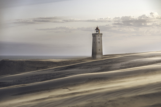 View of Rubjerg Knude lighthouse standing amidst shifting sand dunes under a soft sky in Lokken Denmark. View of Rubjerg Knude lighthouse standing amidst shifting sand dunes under a soft sky in Lokken Denmark.