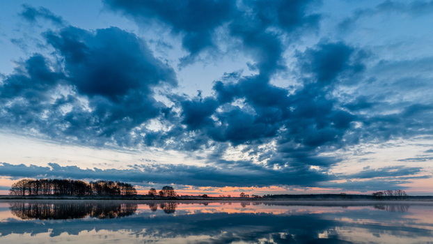 View of a calm lake reflecting a dramatic sunset sky with dark clouds and silhouettes of trees on the horizon in Debrzno Pomeranian Voivodeship Poland. View of a calm lake reflecting a dramatic sunset sky with dark clouds and silhouettes of trees on the horizon in Debrzno Pomeranian Voivodeship Poland.
