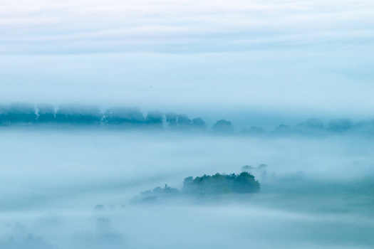Aerial view of rolling hills and dense tree lines shrouded in thick morning mist and low clouds in Nuffield Oxfordshire United Kingdom. Aerial view of rolling hills and dense tree lines shrouded in thick morning mist and low clouds in Nuffield Oxfordshire United Kingdom.