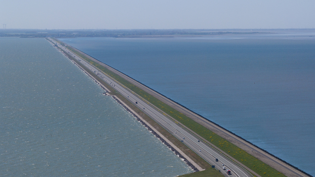 Aerial view of the Afsluitdijk causeway stretching across the water with a highway grassy embankments and calm sea in Breezanddijk Friesland Netherlands.