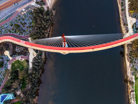 Aerial view of Boorloo Bridge with its distinctive red deck and cable stayed structure spanning the river surrounded by parkland and pathways in East Perth Western Australia Australia.