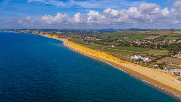Aerial view of West Bay featuring iconic golden sandstone cliffs along the Jurassic Coast with sandy beach blue sea and green landscape in West Bay England United Kingdom. Aerial view of West Bay featuring iconic golden sandstone cliffs along the Jurassic Coast with sandy beach blue sea and green landscape in West Bay England United Kingdom.