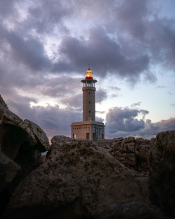 View of Faro de Punta Nariga lighthouse with its lantern lit against a dramatic cloudy sky and jagged coastal rocks in Malpica A Coruna Spain. View of Faro de Punta Nariga lighthouse with its lantern lit against a dramatic cloudy sky and jagged coastal rocks in Malpica A Coruna Spain.