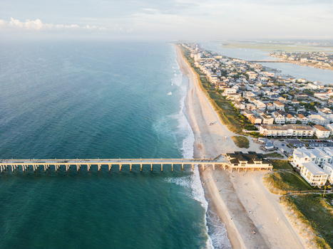 Aerial view of Johnnie Mercers Pier extending into the Atlantic Ocean with sandy beaches and coastal residential buildings in Wrightsville Beach North Carolina United States.