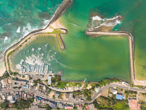 Aerial view of the fishery harbor with fishing boats docked in turquoise waters and stone breakwaters Hikkaduwa Southern Province Sri Lanka. Aerial view of the fishery harbor with fishing boats docked in turquoise waters and stone breakwaters Hikkaduwa Southern Province Sri Lanka.
