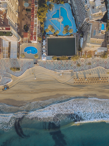 Aerial view of a coastal resort with swimming pools a patterned promenade and sandy beach meeting the turquoise sea in Calp Valencian Community Spain. Aerial view of a coastal resort with swimming pools a patterned promenade and sandy beach meeting the turquoise sea in Calp Valencian Community Spain.
