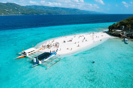 Aerial view of the white sandbar at Sumilon Island with turquoise water traditional outrigger boats and people relaxing on the beach in Oslob Central Visayas Philippines. Aerial view of the white sandbar at Sumilon Island with turquoise water traditional outrigger boats and people relaxing on the beach in Oslob Central Visayas Philippines.
