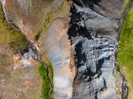Aerial view of the geothermal valley of Grensdalur featuring rugged rocky slopes steaming vents winding streams and vibrant green mossy vegetation in Sveitarfelagid Olfus Iceland. Aerial view of the geothermal valley of Grensdalur featuring rugged rocky slopes steaming vents winding streams and vibrant green mossy vegetation in Sveitarfelagid Olfus Iceland.