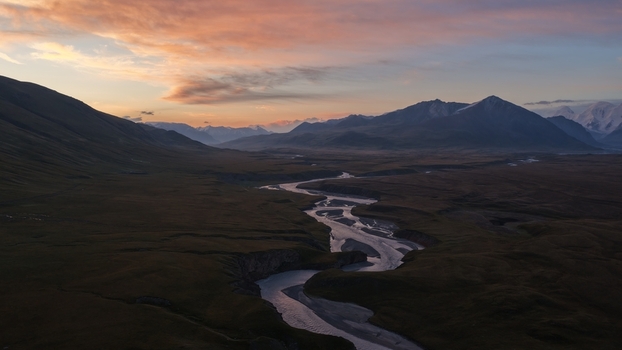 Aerial view of the winding river flowing from the Engilchek Glacier through the vast mountainous landscape during a golden sunset in Ak Su Issyk Kul Region Kyrgyzstan. Aerial view of the winding river flowing from the Engilchek Glacier through the vast mountainous landscape during a golden sunset in Ak Su Issyk Kul Region Kyrgyzstan.