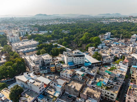 Aerial view of the dense urban landscape of Udaipur featuring residential buildings flat rooftops and lush green trees under a clear sky in Udaipur Rajasthan India.