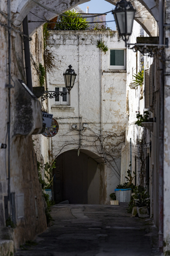 View of a narrow alleyway with white washed stone walls and traditional street lamps in the historic center of Ostuni Apulia Italy. View of a narrow alleyway with white washed stone walls and traditional street lamps in the historic center of Ostuni Apulia Italy.