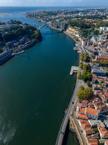 Aerial view of Viaduto do Cais das Pedras spanning the Douro River with historic buildings lush trees and urban infrastructure along the waterfront in Porto Porto Portugal. Aerial view of Viaduto do Cais das Pedras spanning the Douro River with historic buildings lush trees and urban infrastructure along the waterfront in Porto Porto Portugal.