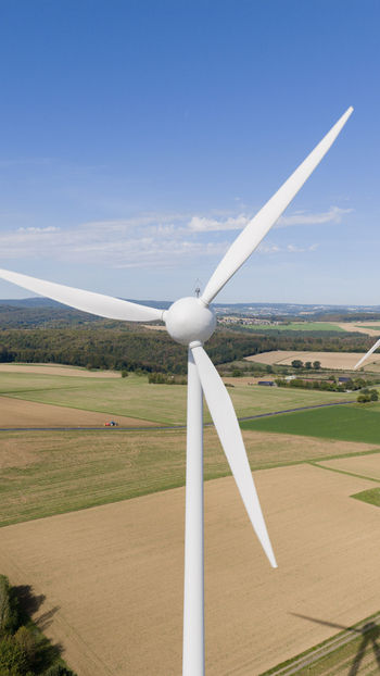 Aerial view of Windpark Eppenrod featuring a white wind turbine in a rural landscape with agricultural fields rolling hills and a clear blue sky in Eppenrod Rheinland Pfalz Germany.